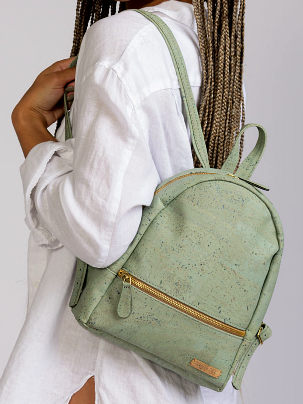 Woman wearing a mint green backpack with gold zipper and carrying it.