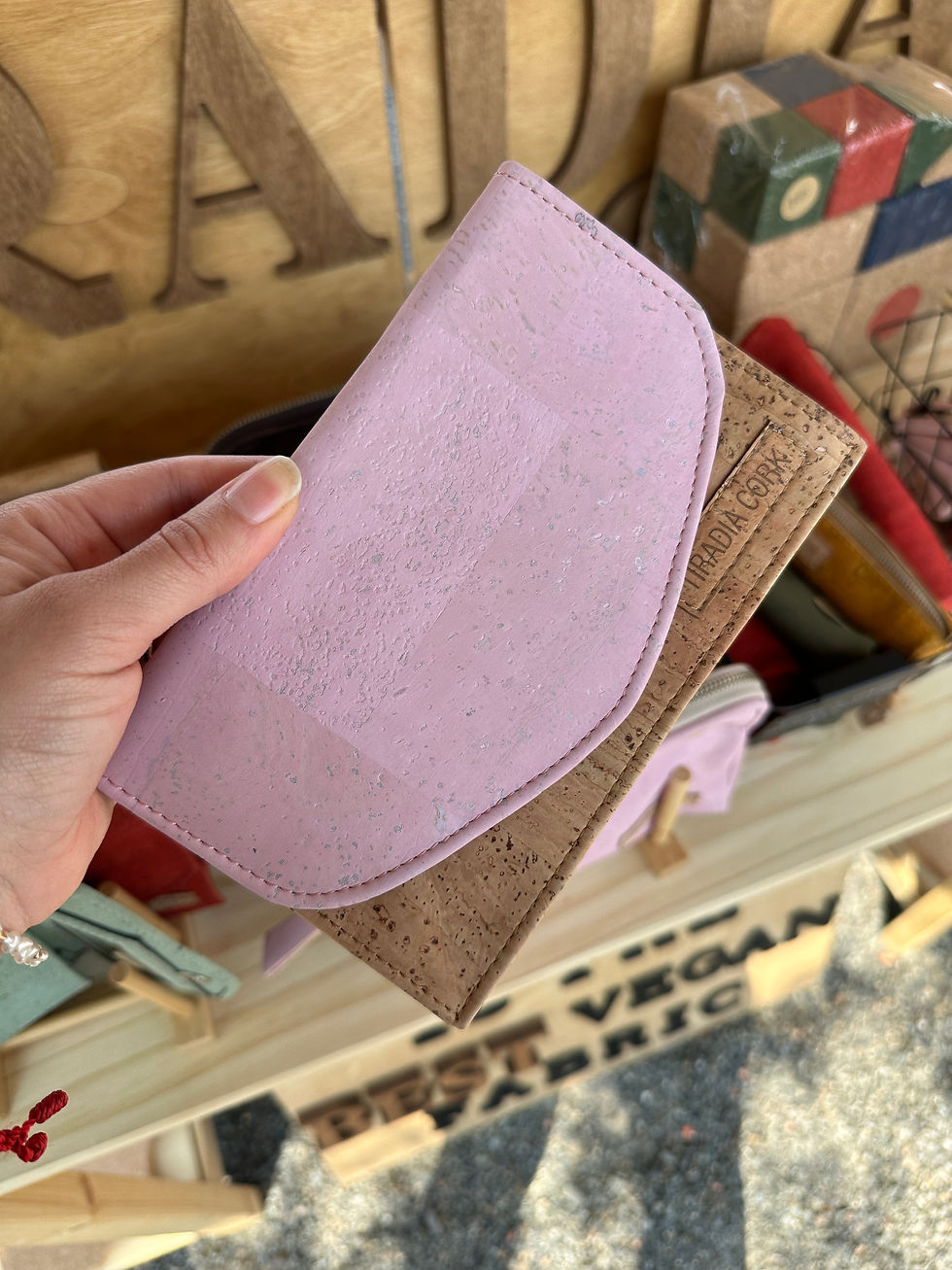 Hand holding a light purple wallet with Vegan Fabric text, and a cork wallet.