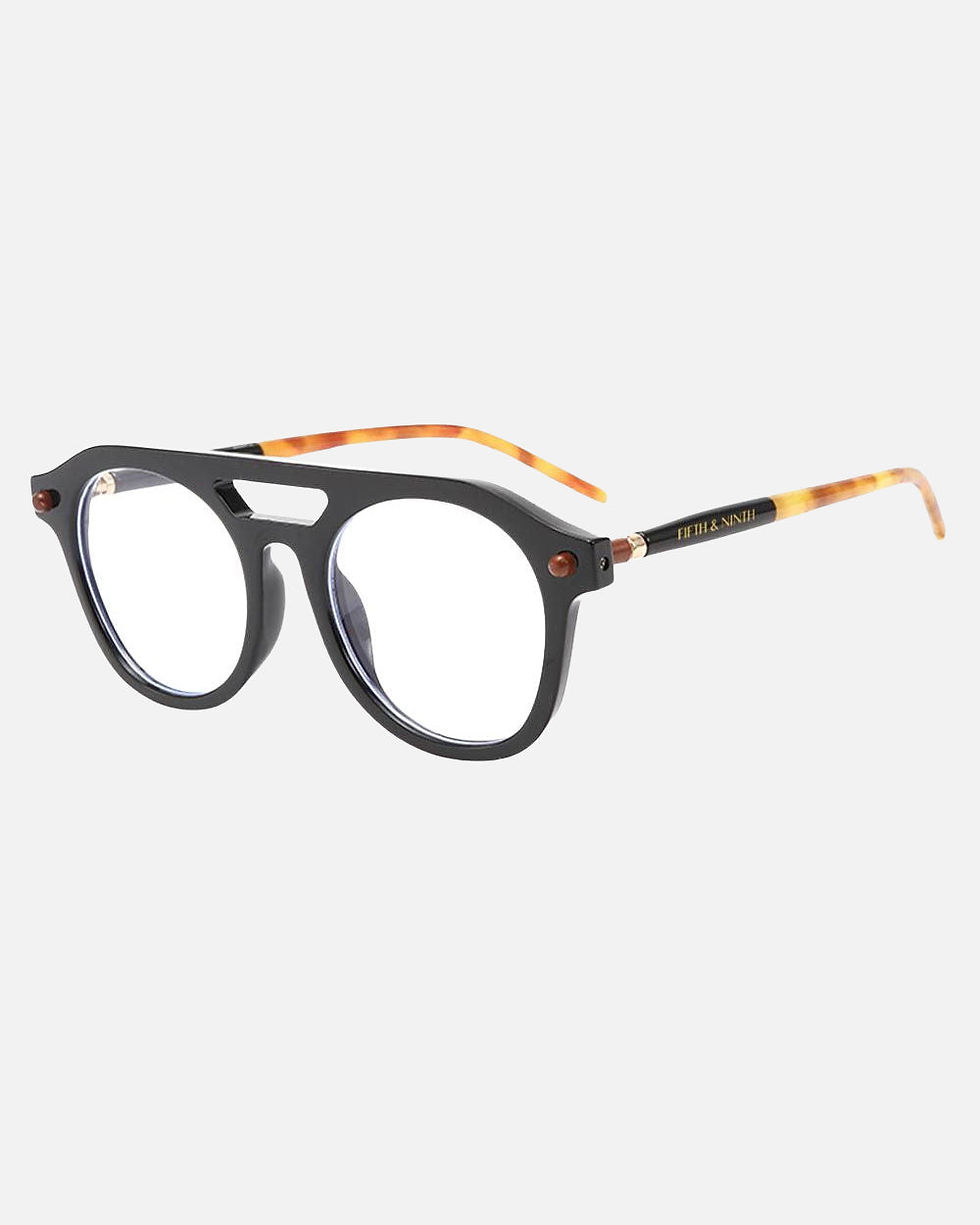 Black eyeglasses with round lenses and brown arms on a light surface Khaam Fefalene
