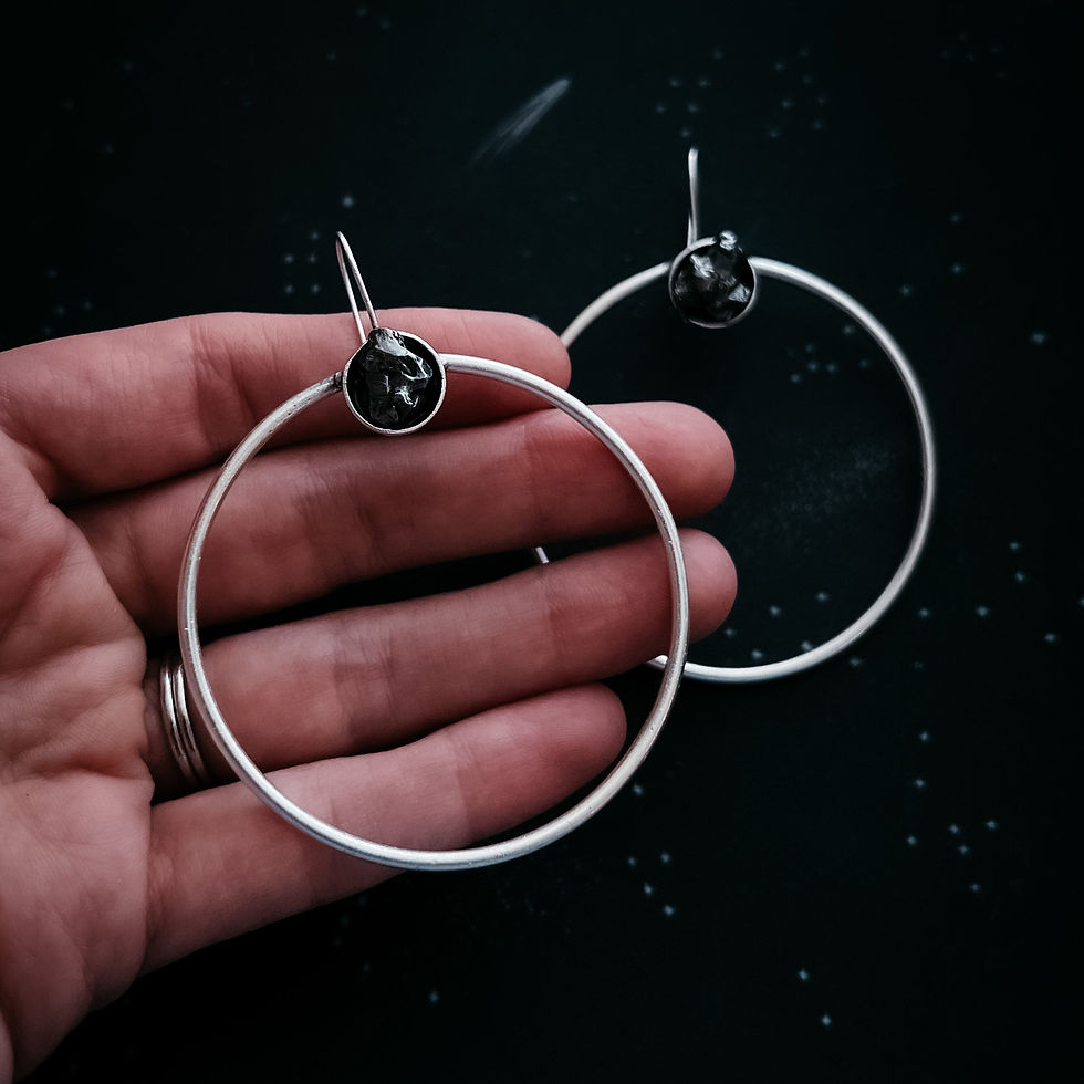 Hand holding large silver hoop earrings with dark stone accents against black background.