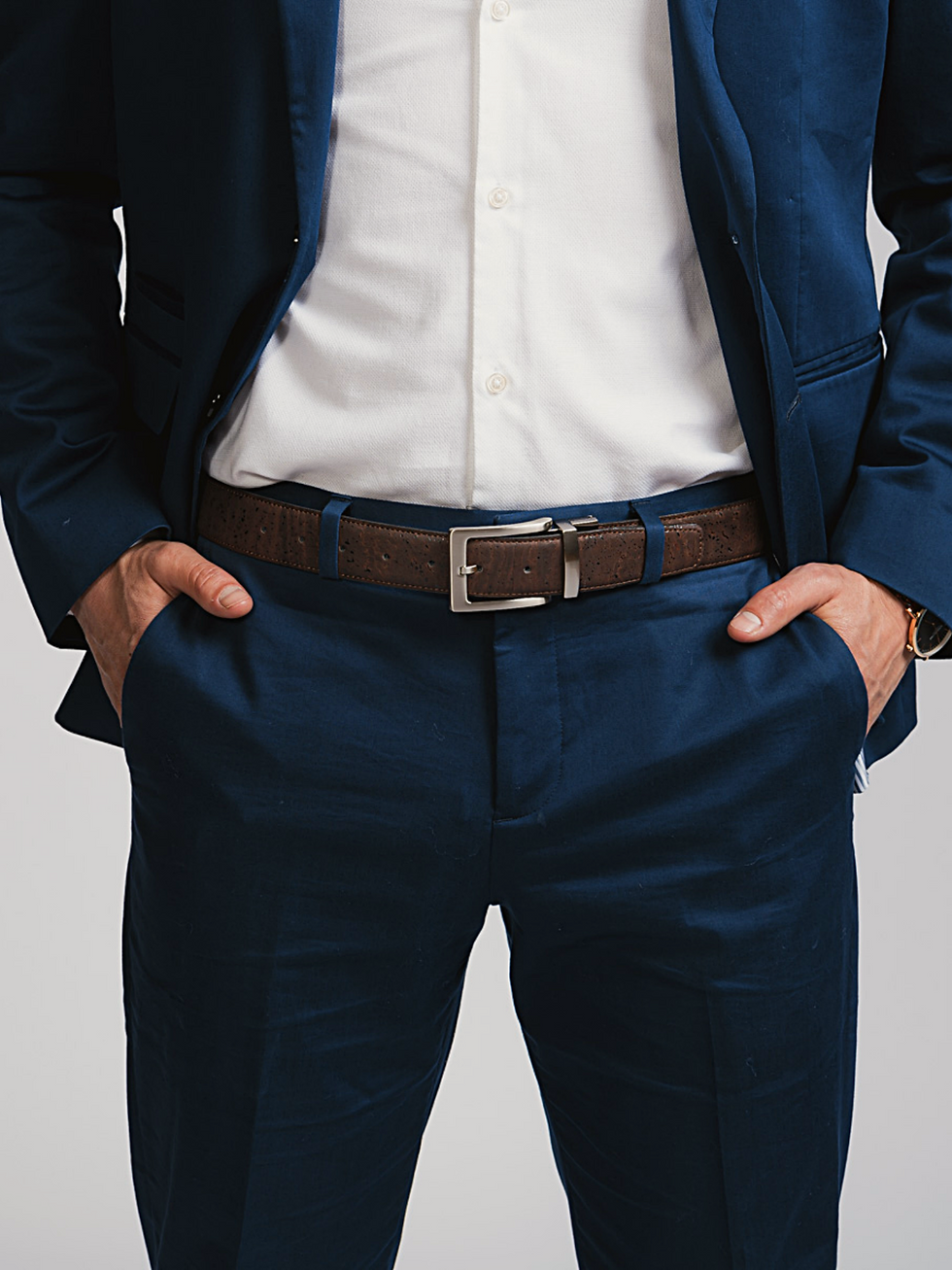 Man in blue suit with hands in pockets, brown belt and white shirt.