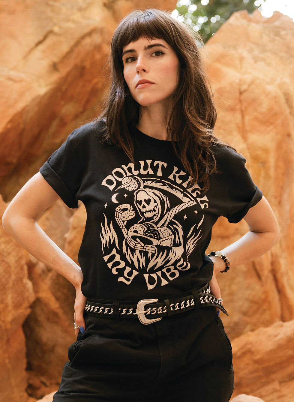 Woman wearing a black T-shirt with "DONUT KILL MY VIBE" graphic in desert setting.