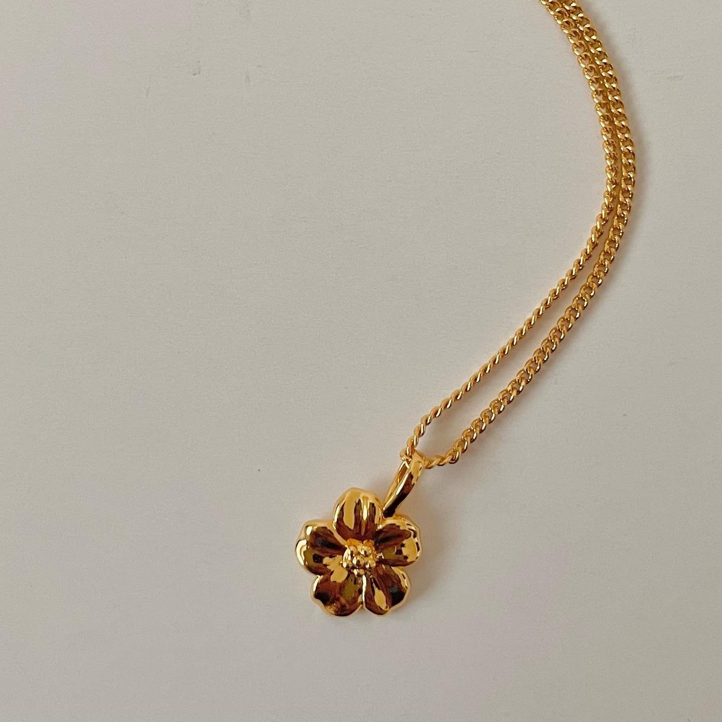 Golden flower pendant necklace on white surface. Elegant jewelry piece for women.