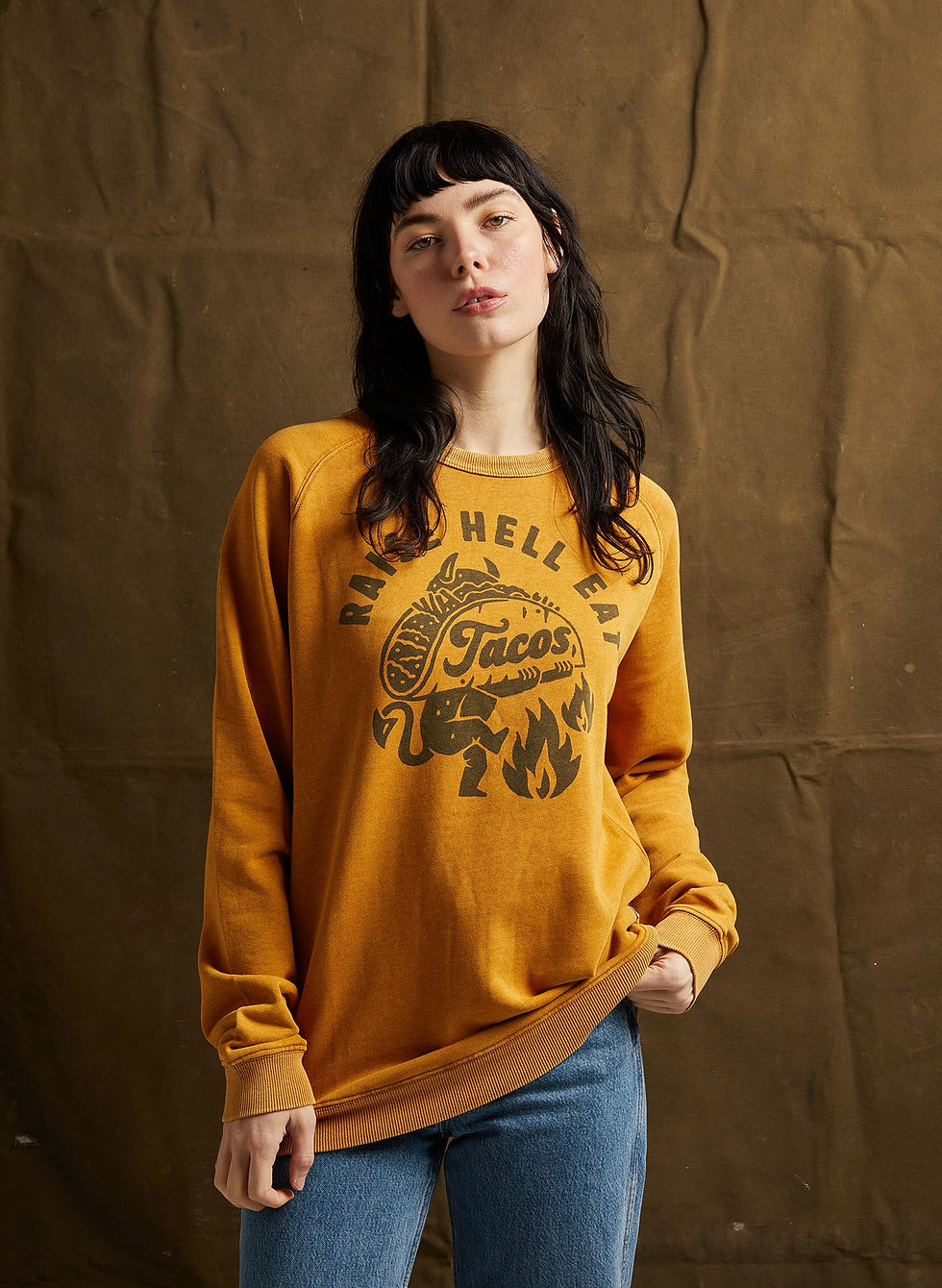 Woman wearing yellow sweatshirt with Taco Hell text, looking at the camera.