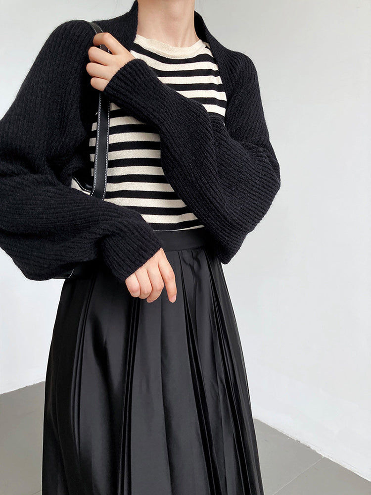 Woman wearing black sweater, striped shirt, and pleated black skirt, Khaam Fefalene.