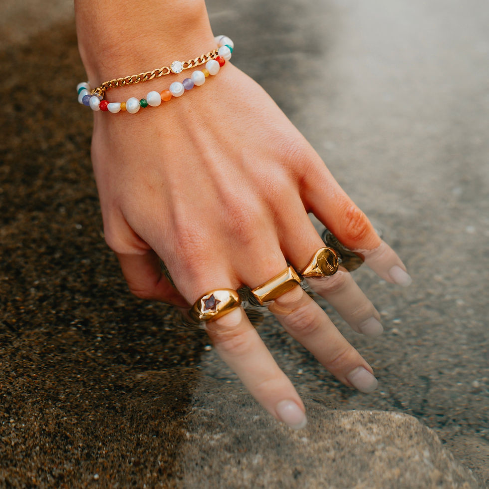 Woman's hand with gold rings and bracelet, touching water at the beach.