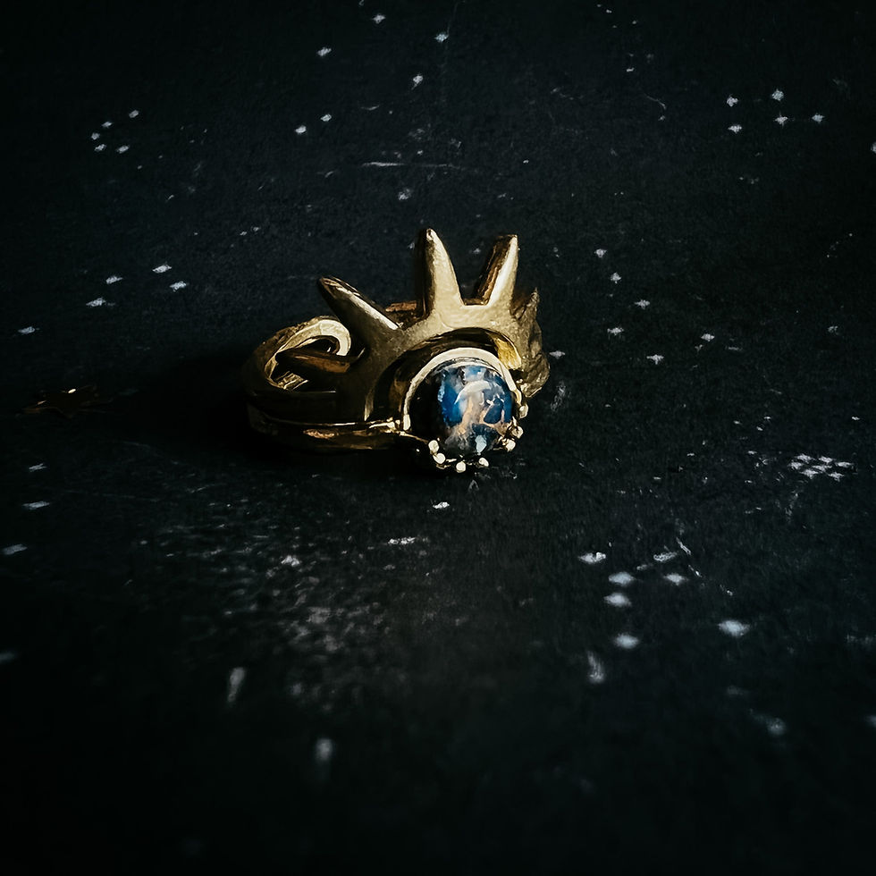 Gold ring with blue gem and sun design set against a dark background.