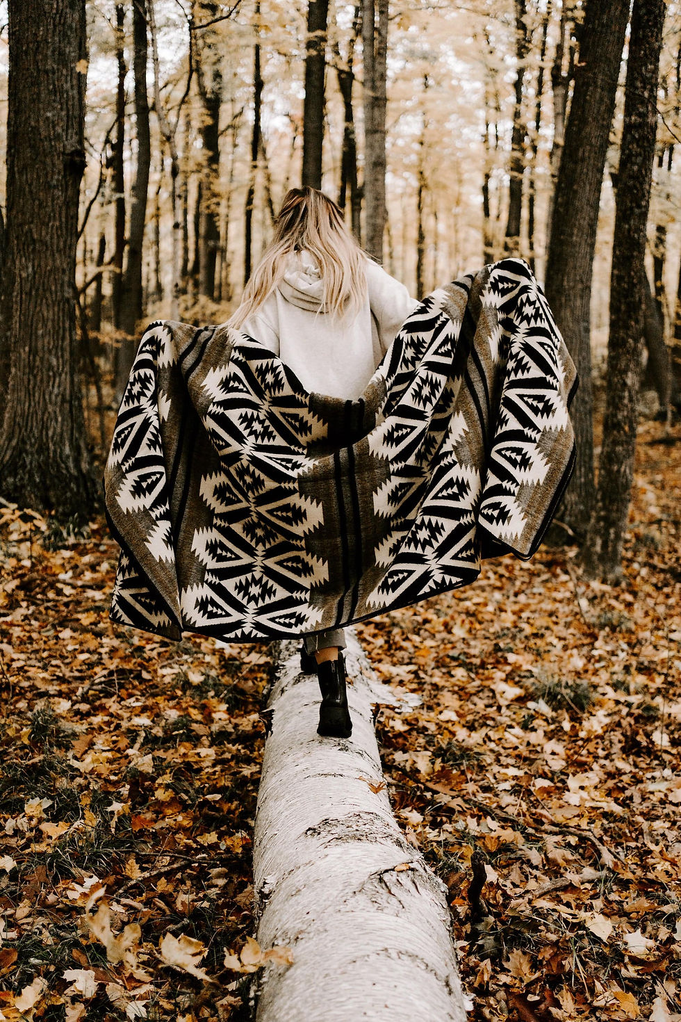 Woman wearing patterned shawl stands on a tree trunk in a forest