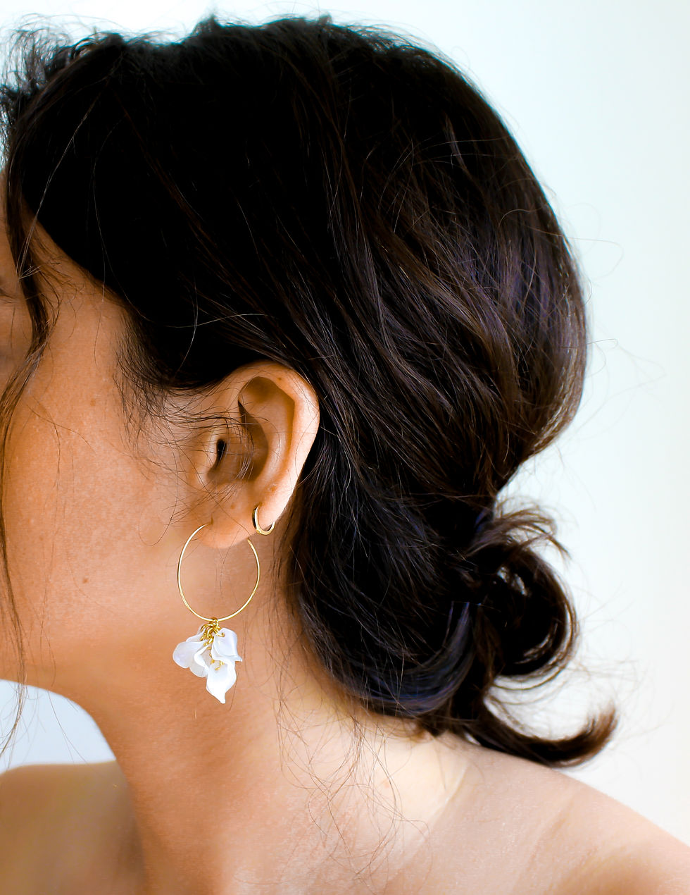 Woman wearing gold hoop earrings with white floral pendant detail