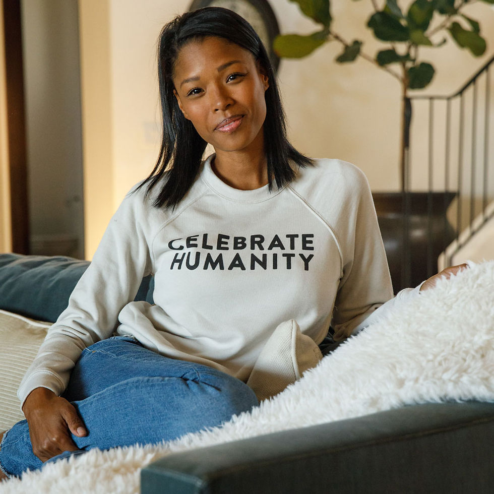 Woman wearing CELEBRATE HUMANITY SWEATSHIRT | CREWNECK, sitting comfortably on a sofa, looking at the camera