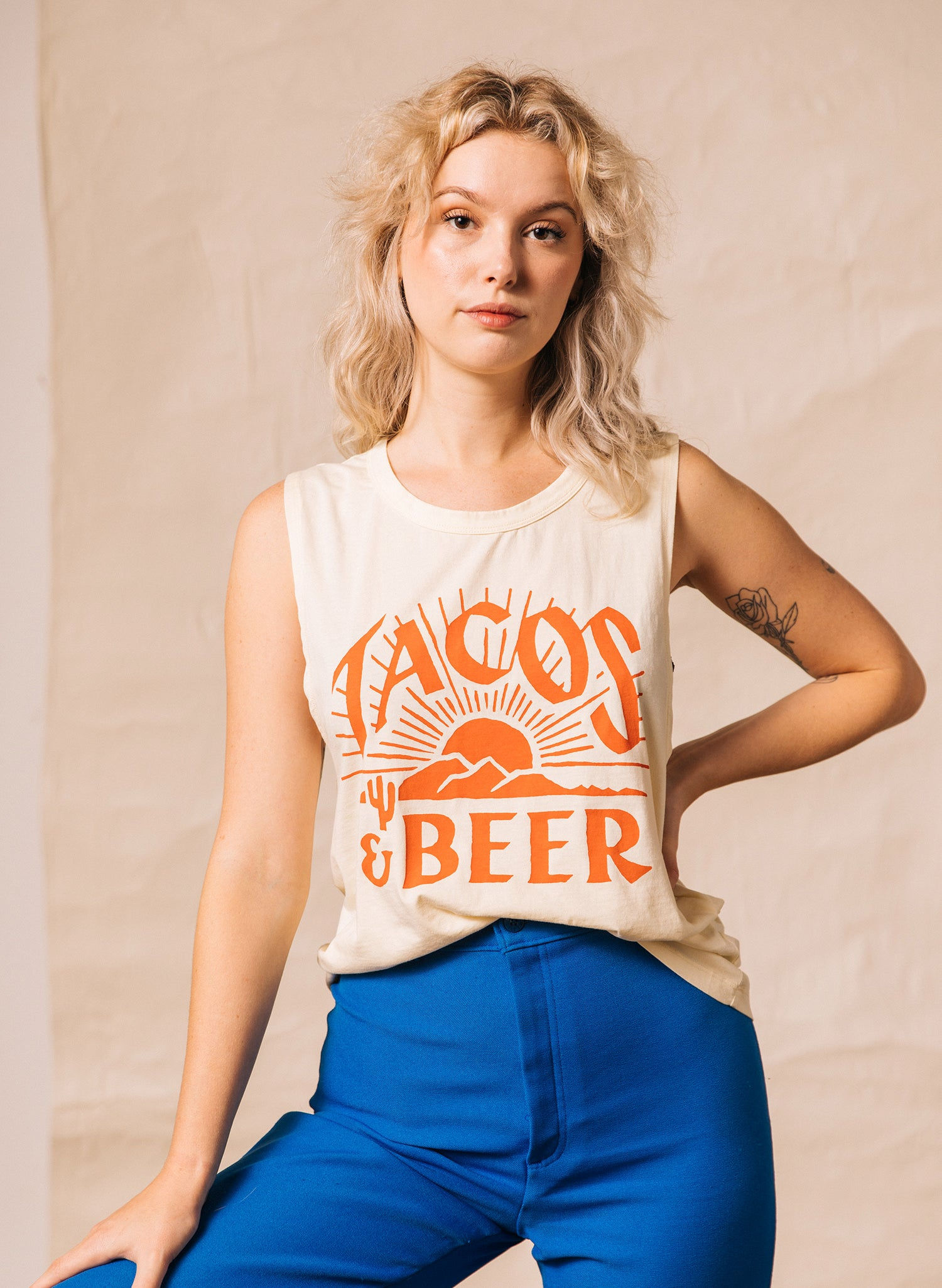 Young woman wearing a cream tank top with "TACOS & BEER" printed on it.