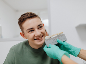 young man smiling as dentist holds up matching tooth color samples