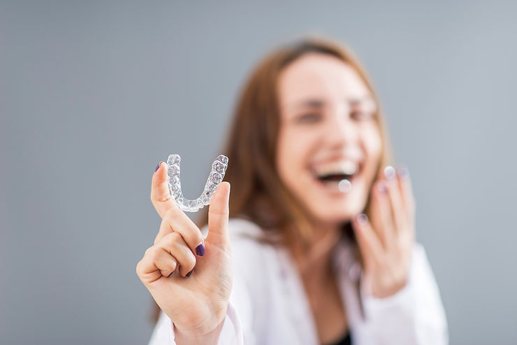 woman smiling and holding an Invisalign aligner
