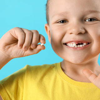 young boy holding a lost baby tooth as he smiles showing off his missing teeth