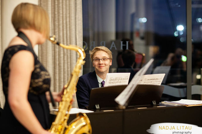 A pianist and saxophonist smile at each other.