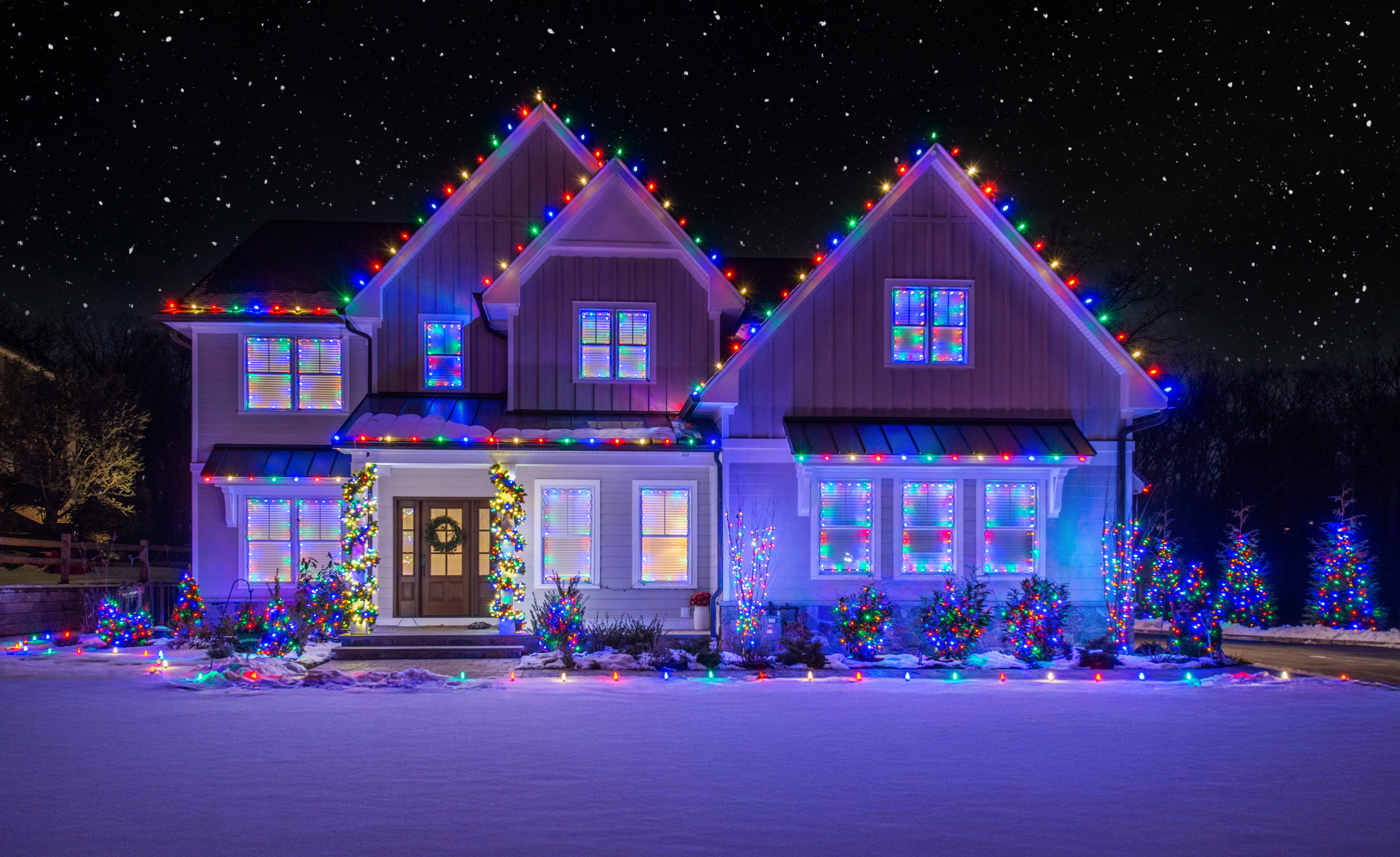 Two-story home with blue and purple roofline lights and multicolor window and shrub lights