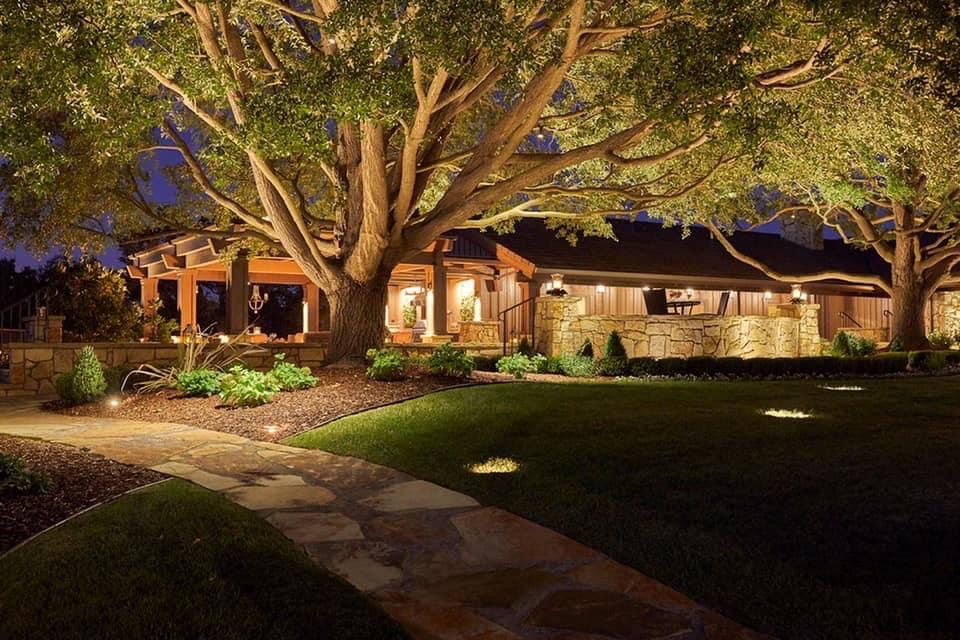 Large oak tree uplit beside a lit home
