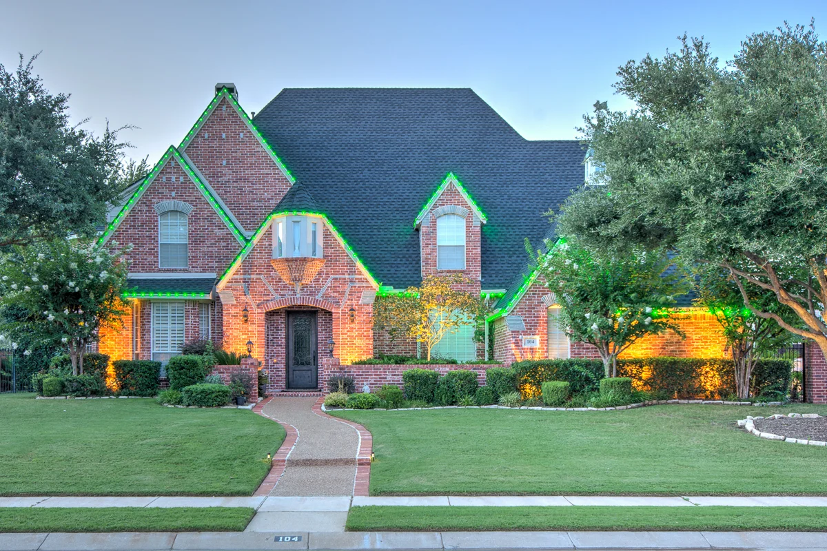 Permanent green accent lighting outlining the gables of a brick home