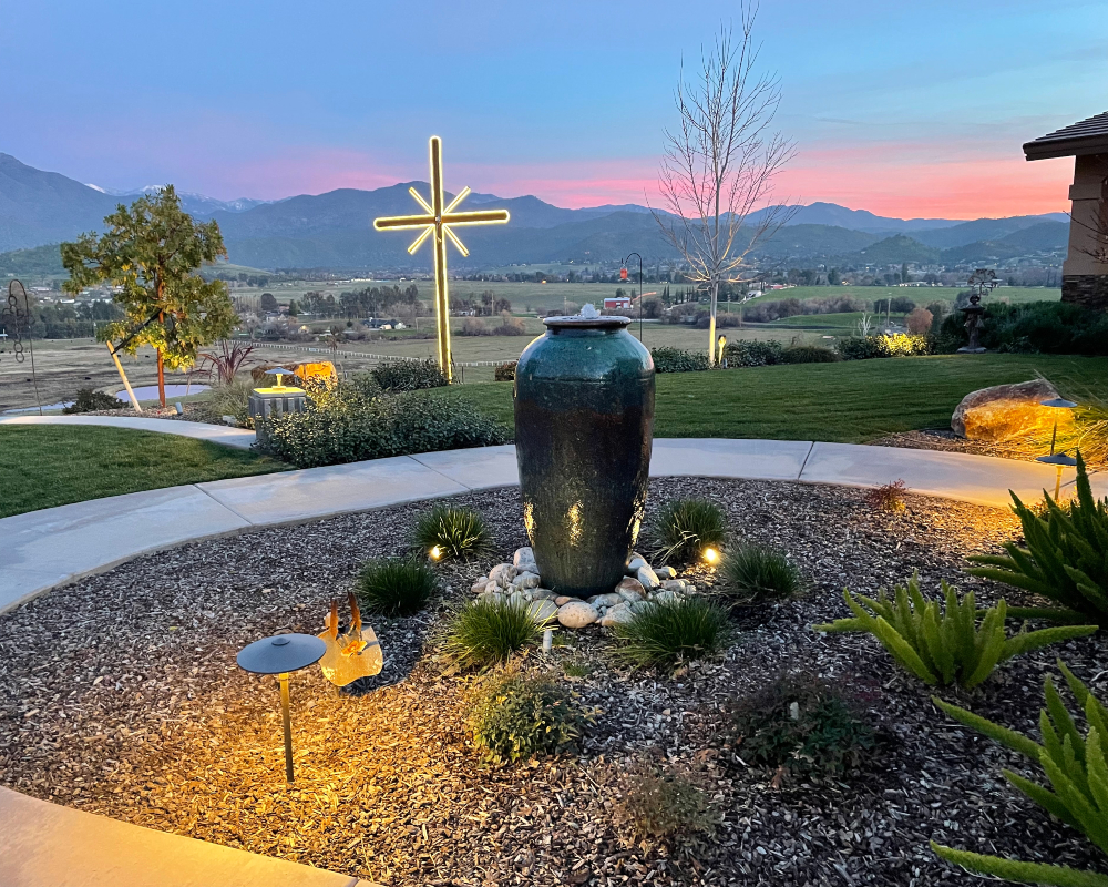 Lit fountain and garden path at sunset with foothills behind