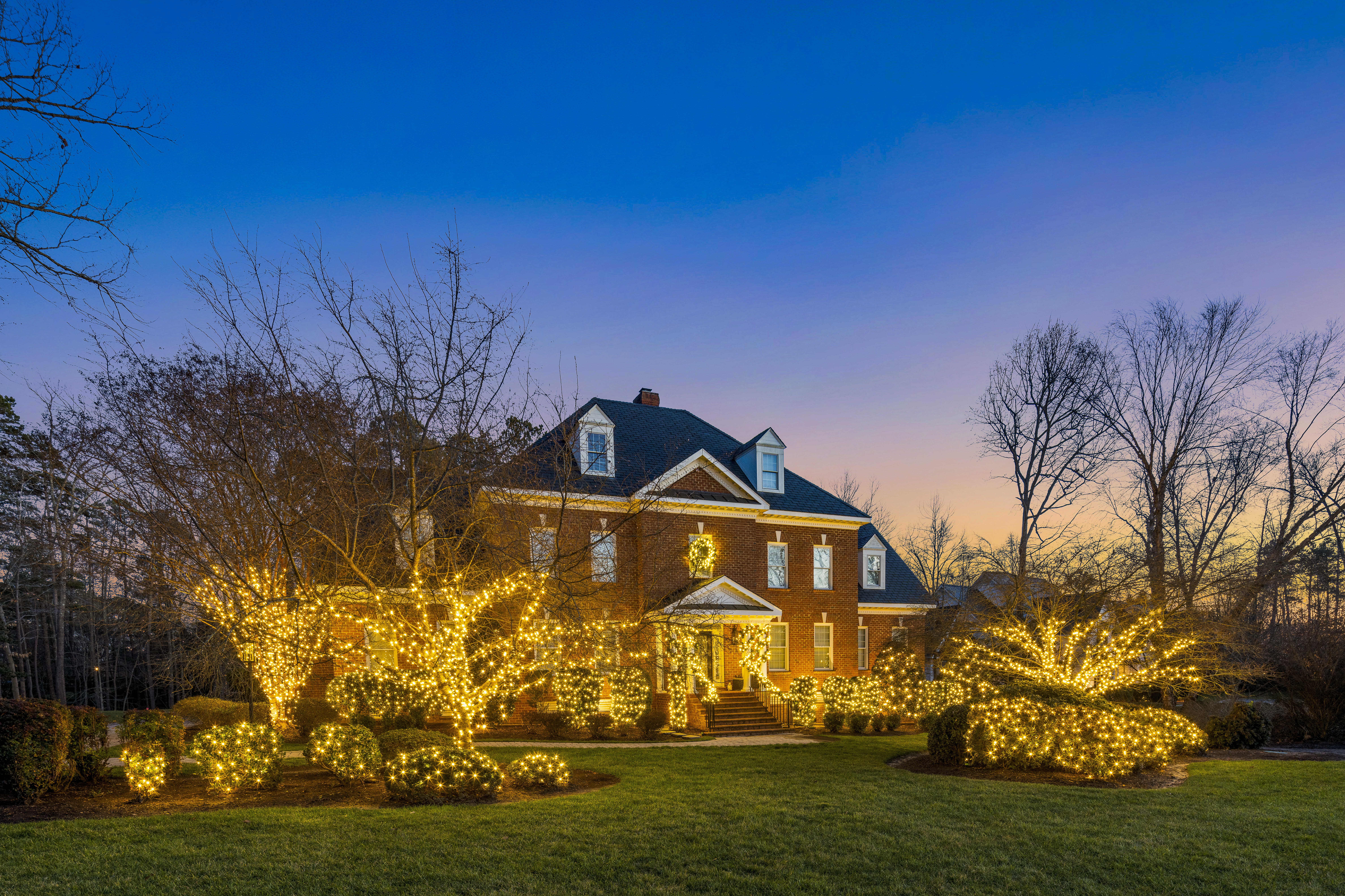Brick colonial home with lit trees