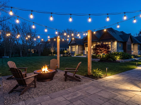 Bistro string lights over a backyard fire pit seating area at dusk
