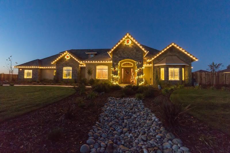 Customer home with a warm-white Christmas roofline and lit entry garland at dusk