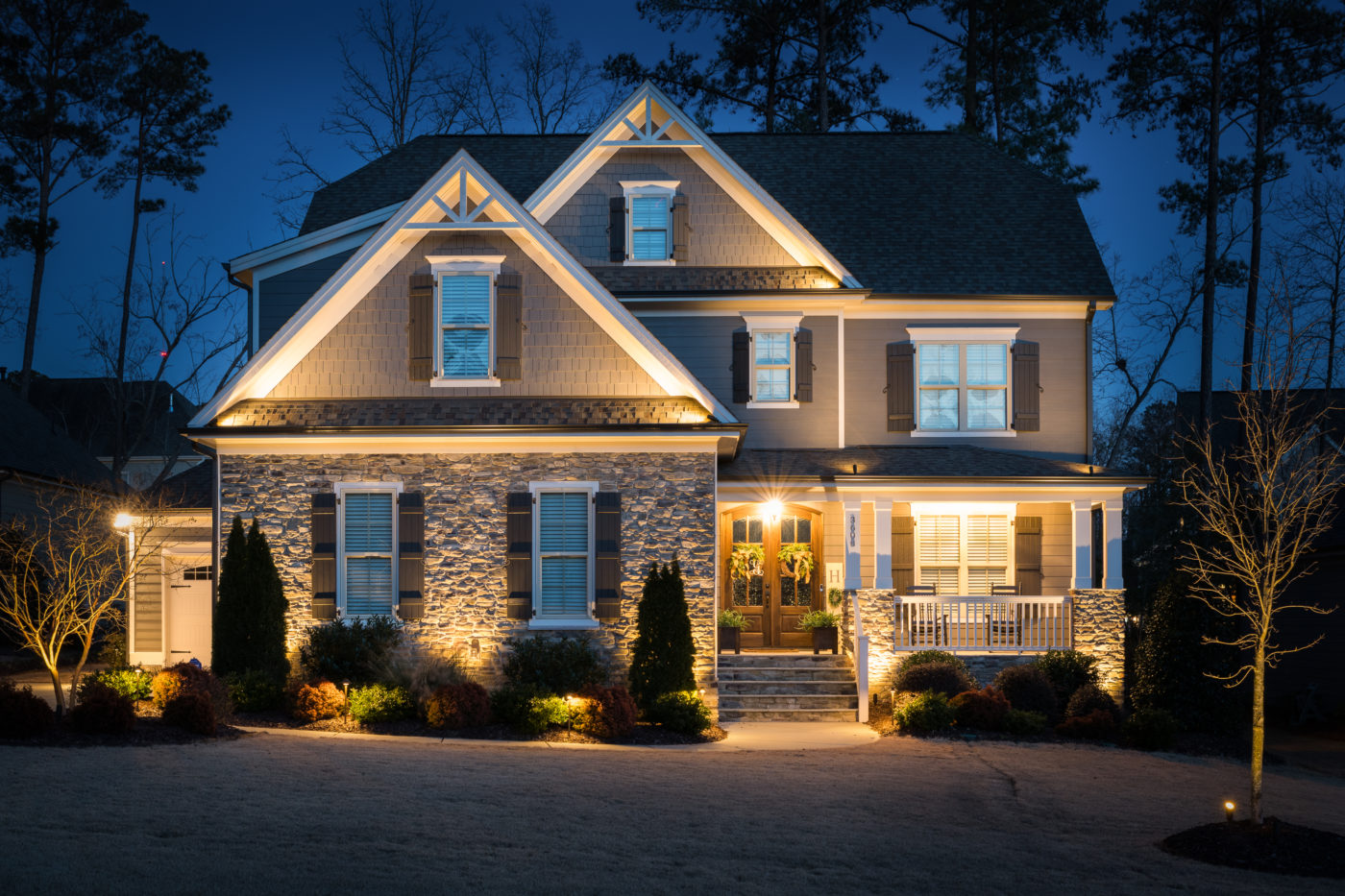 Two-story home with warm uplighting on the facade and trees