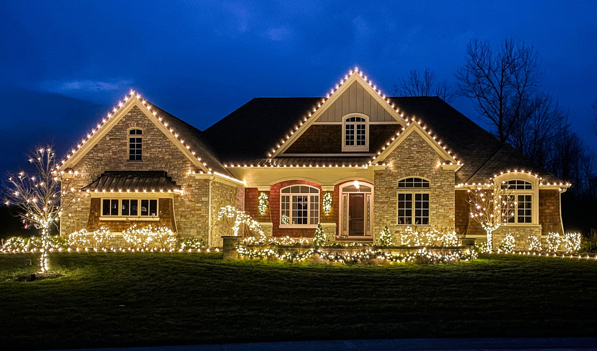 Brick two-story home with a warm-white roofline and lit trees