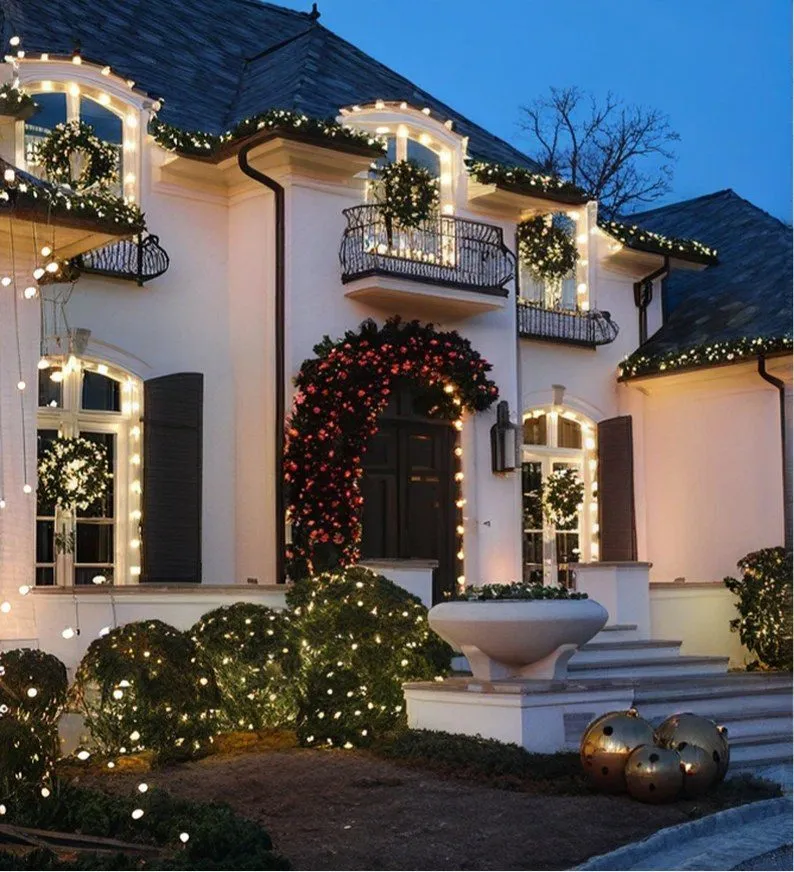 White estate home with wreaths, garland and warm white lights over the front entry