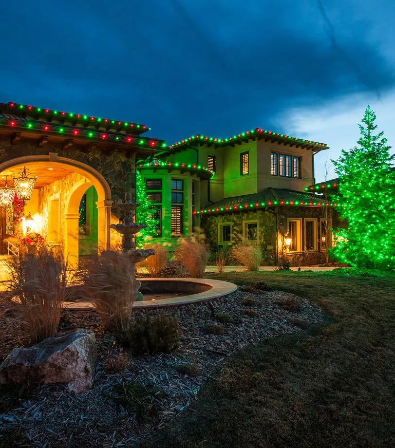 Home with green roofline lighting and lit trees and landscaping