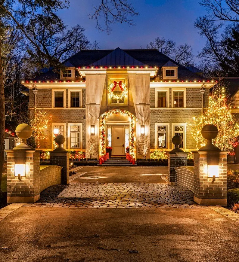 Estate home with warm white roofline lights, lighted garland and a lit front courtyard