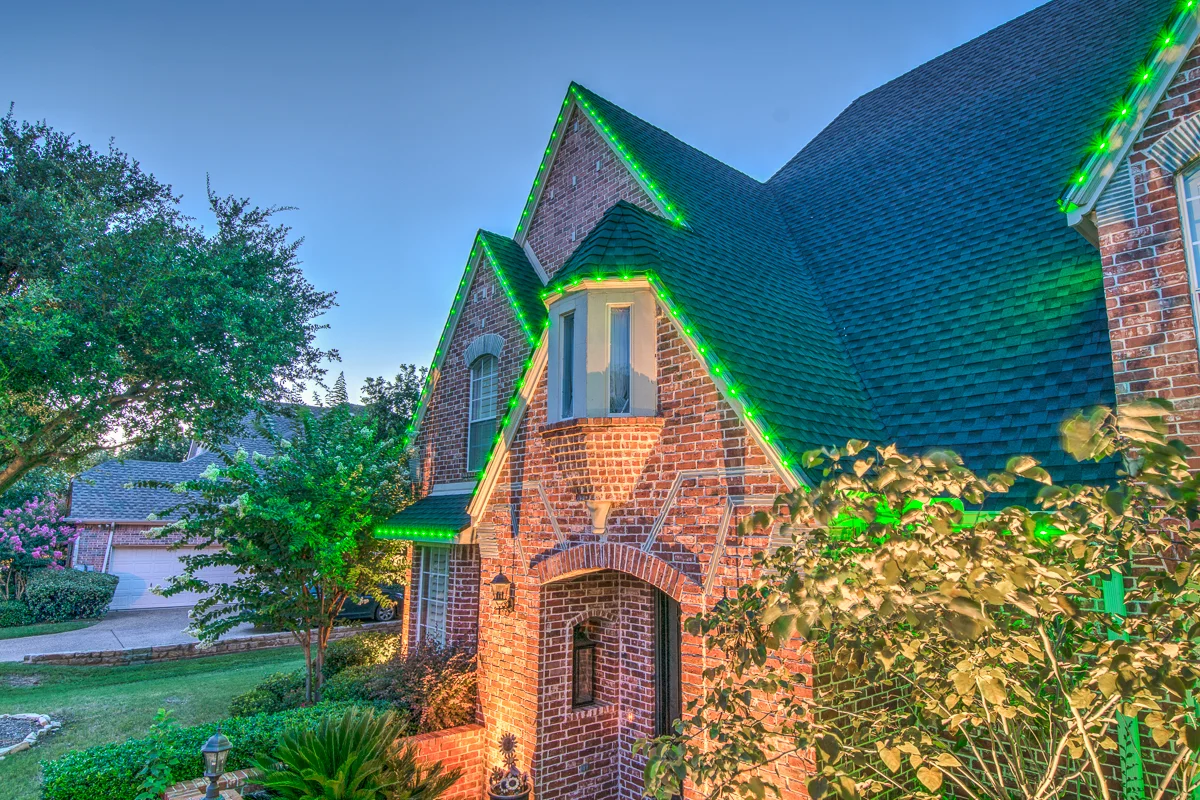Permanent green roofline lighting on a brick home's steep gables