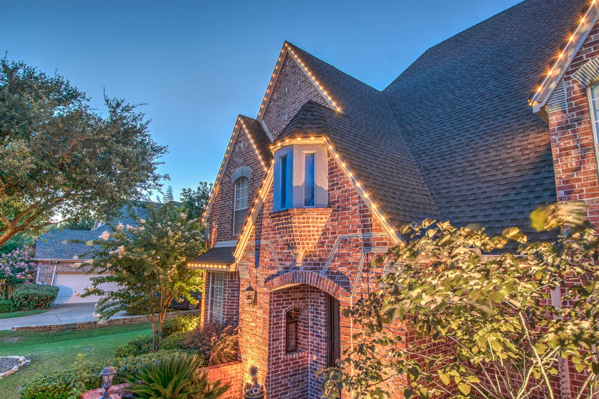 Permanent warm white lighting tracing the roofline of a brick home at dusk