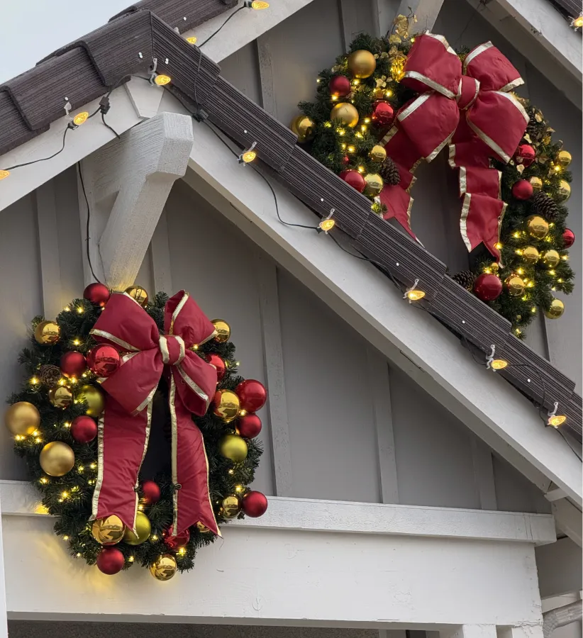 Porch gable decorated with red-bow Christmas wreaths and roofline lights
