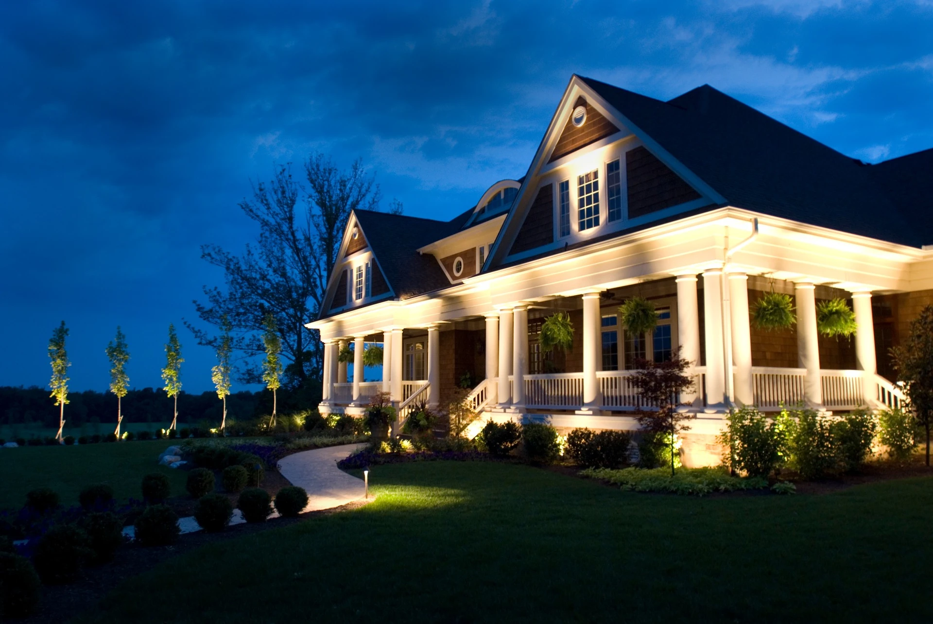 White two-story home with path lights and landscape uplighting at dusk
