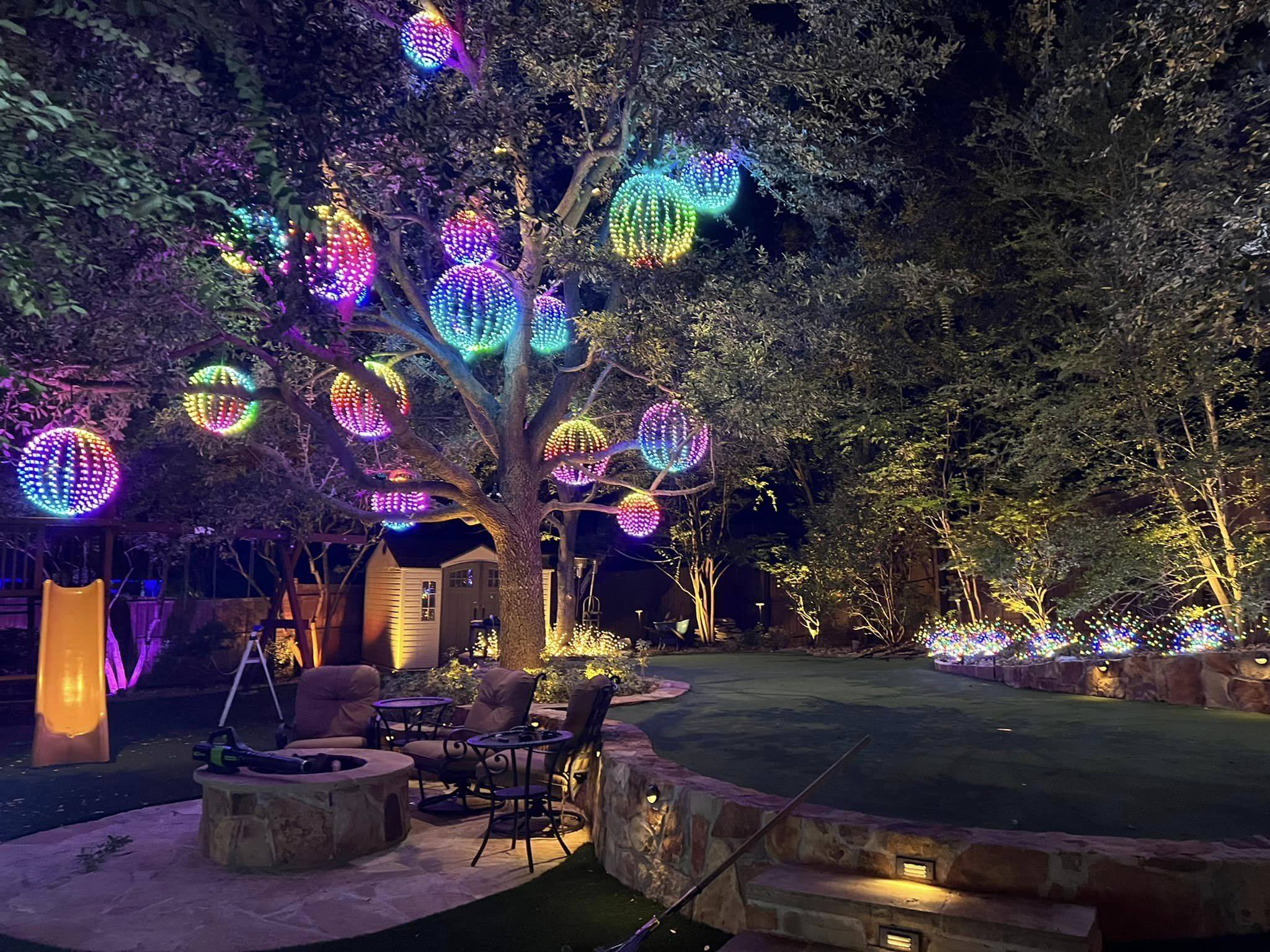 Tree hung with color-changing light spheres over a patio