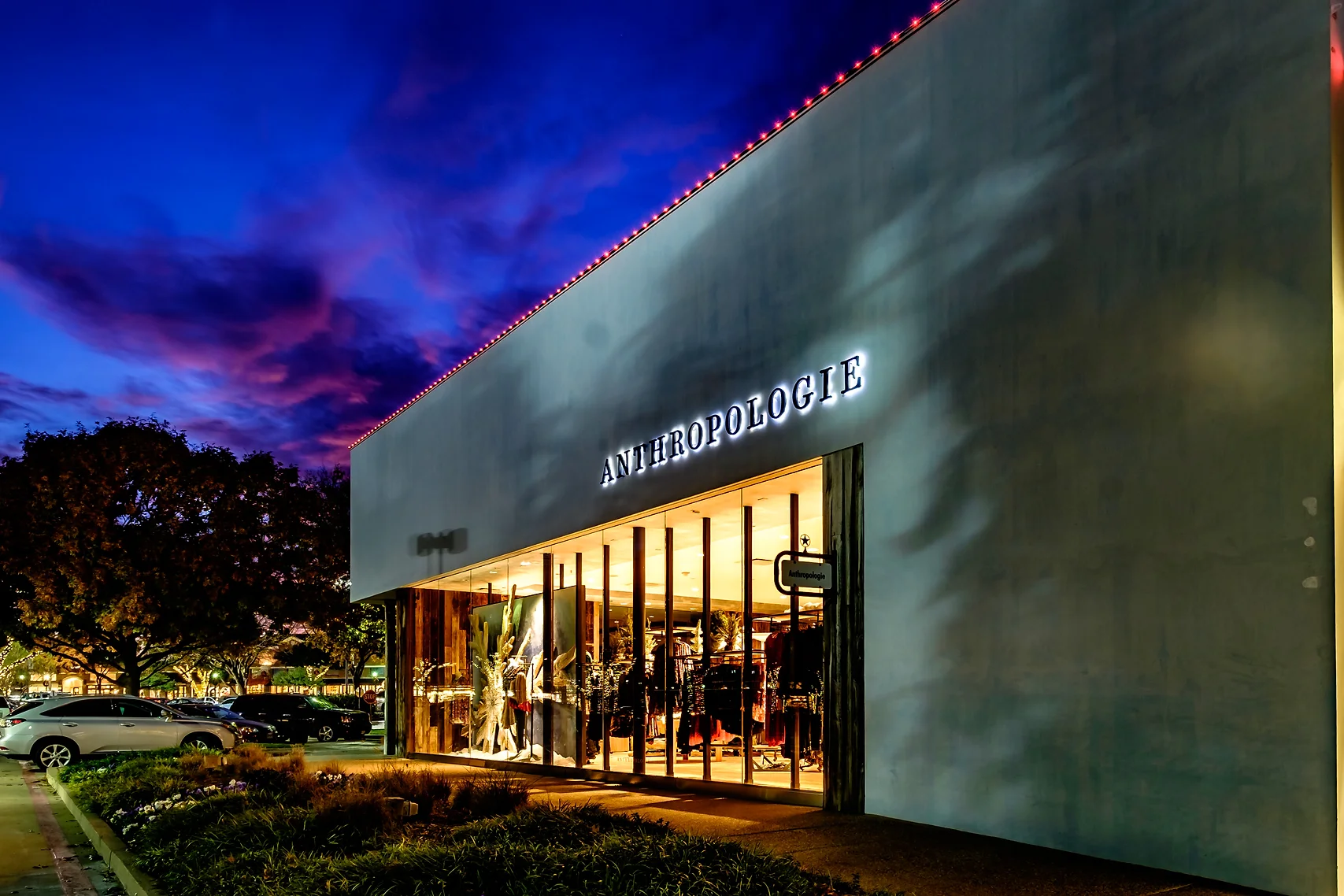 Permanent pink and white lighting along a retail building parapet at dusk