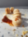 Macarons mit Karamellfüllung auf dem weißen Hintergrund mit Creme, Karamell und Waffelstückchen im Hintergrund