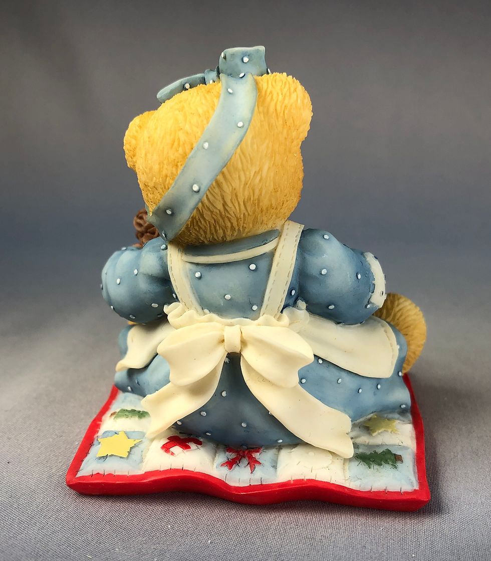 Thumbnail: Girl bear sitting on a quilt while holding a snowman in a basket and a wreath rear view