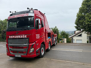 Camion de dépannage rouge Volvo de Mecano Service FC stationné sur route goudronnée avec maisons en arrière-plan à Besançon