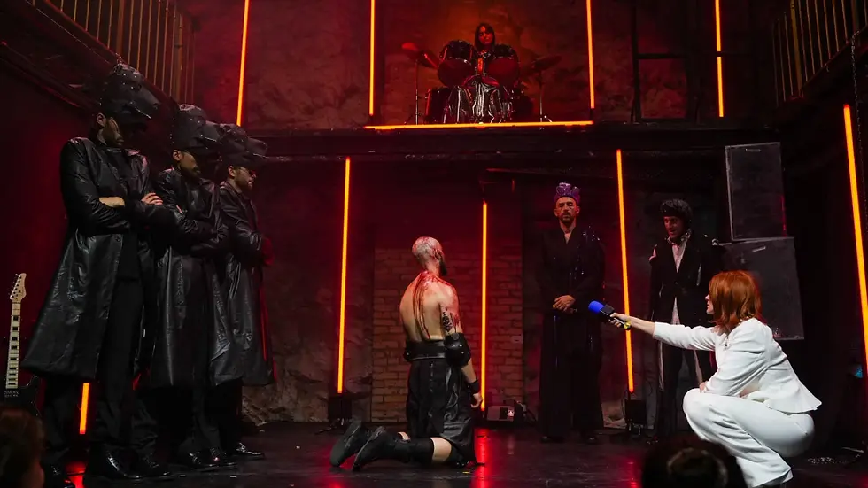 Photographie de scène du spectacle "Hercule" par le Collectif Nox, montrant plusieurs comédiens en costumes sombres et futuristes sur un plateau éclairé par des tubes verticaux orange, avec un batteur installé en hauteur en arrière-plan.