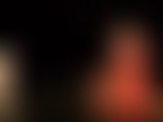 La comédienne Isabelle Andréani, en robe d'époque rouge et dorée, sourit assise près d'une malle en bois, face au buste sculpté de Molière sur une scène sombre.