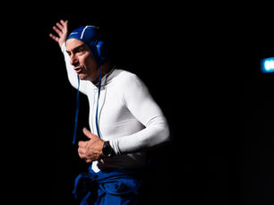 Photographie de scène en clair-obscur montrant le comédien Yohann Métay en haut blanc moulant et bonnet de bain bleu, le bras levé et le regard expressif, se détachant sur un fond noir de théâtre.