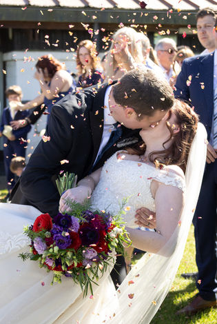 Groom dips bride for a kiss as confetti falls at their wedding