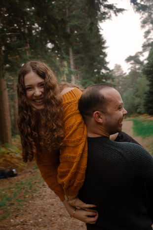 Smiling man giving woman piggyback ride in forest