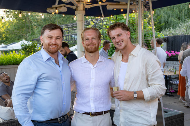 Three men smiling at an outdoor wedding celebration.