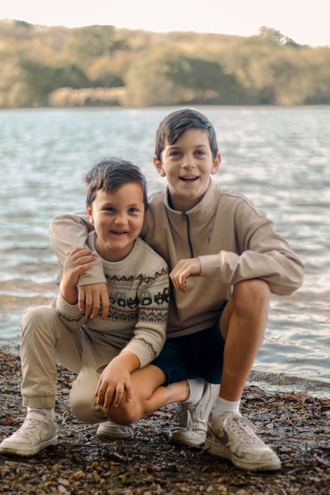 Two smiling boys crouching together by a lake