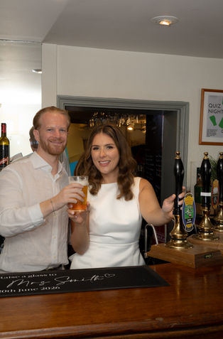 Bride and groom posing behind a bar with a pint of beer.