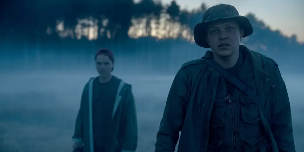 Szenenbild aus Staffel 1 von „Oderbruch“: Zwei Figuren stehen in nebliger Landschaft am Waldrand, die Atmosphäre ist düster und angespannt.