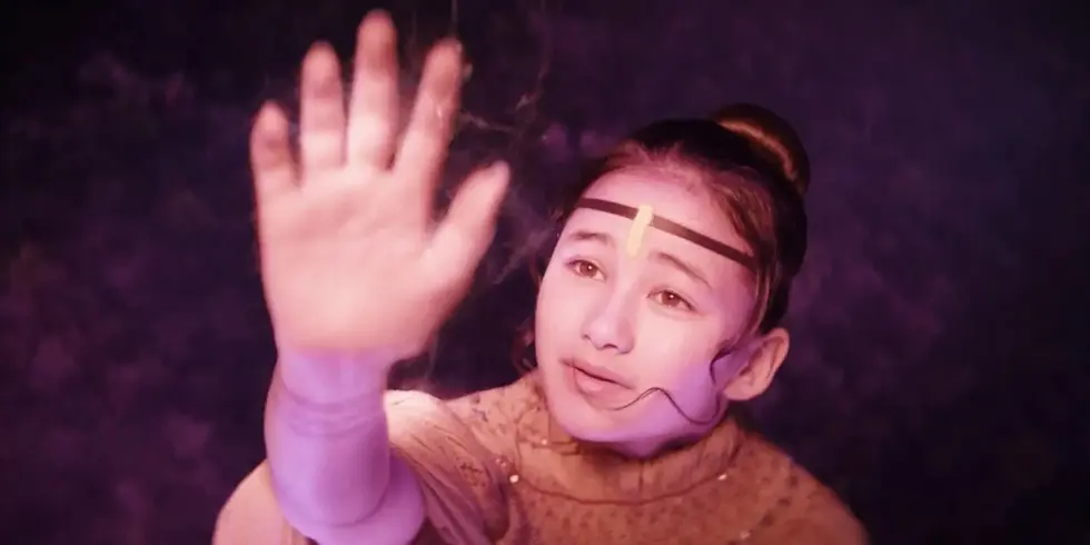 Kaylee Hottle als Jia hebt in einer rötlich beleuchteten Szene aus „Godzilla x Kong: The New Empire“ die Hand.